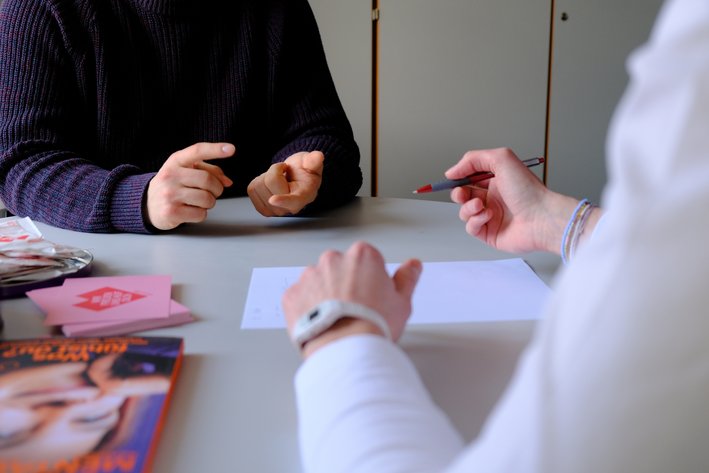 Vertrauliche Beratungssituation. Hände zweier Personen am Tisch, einer schreibt.
