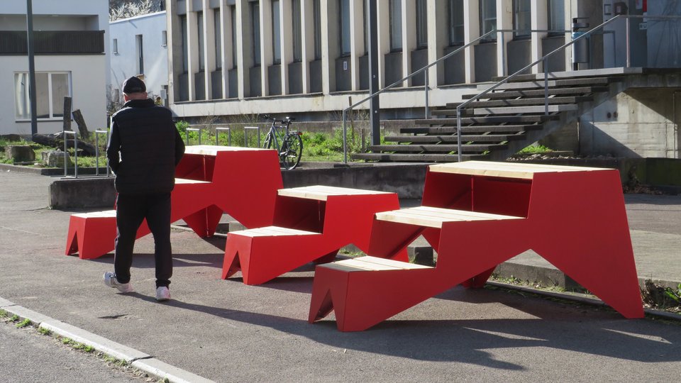 Drei rote Sitzmöbel der Produktlinie STOOP auf Gehweg vor Haus 5 der Hochschule
