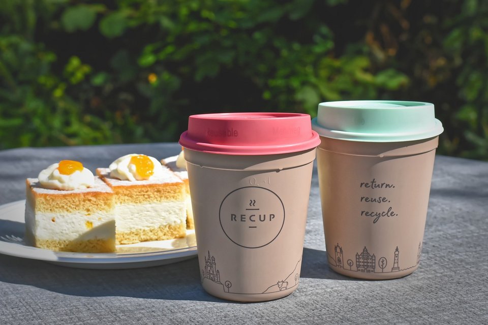 Zwei Kaffeebecher und drei Stück Mandarinenkuchen