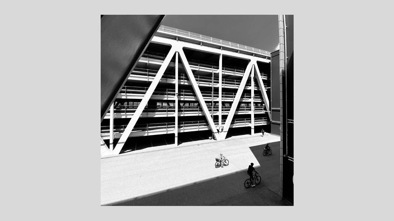 Schwarzweiß Architekturfotografie einer Straßenszene mit Fahrradfahrern und Parkhaus im Hintergrund