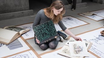 Studierende schaut auf dem Boden sitzend Zeichnungen an