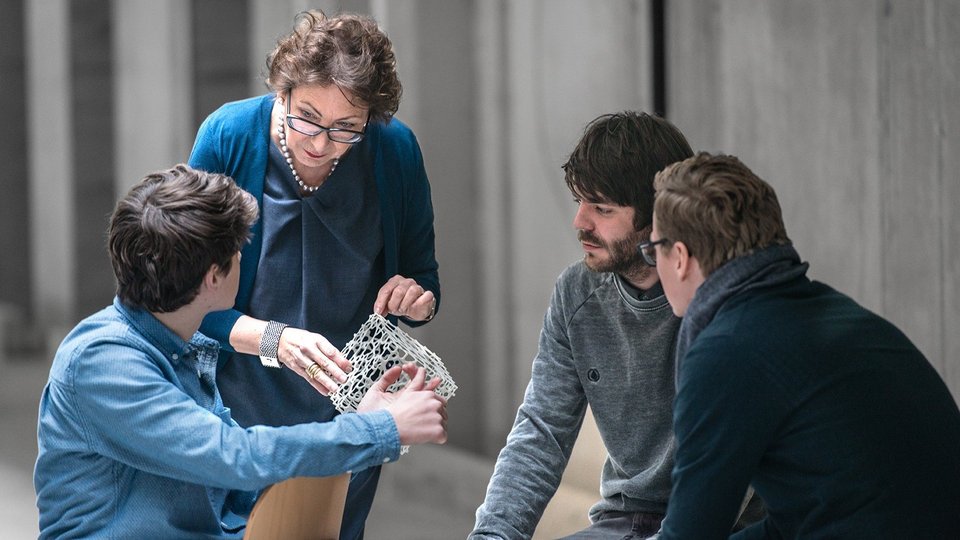 Drei Studierende sprechen mit Professorin über ein Modell 