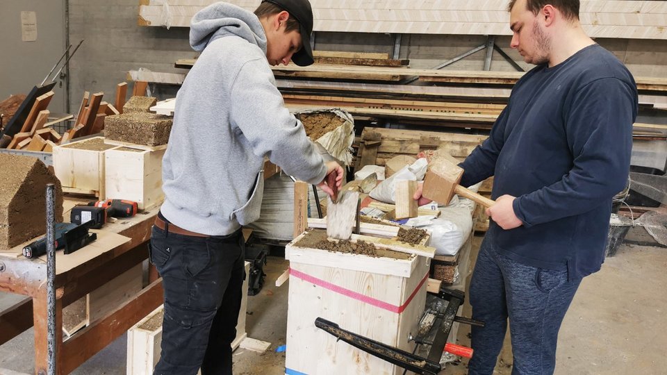 Studierende bei der Bearbeitung der Holzschalung eines Stampflehmmodells