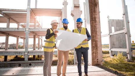 Drei Personen betrachten einen Bauplan auf einer Baustelle