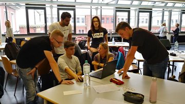 Sechs Studierende diskutieren vor einem Laptop