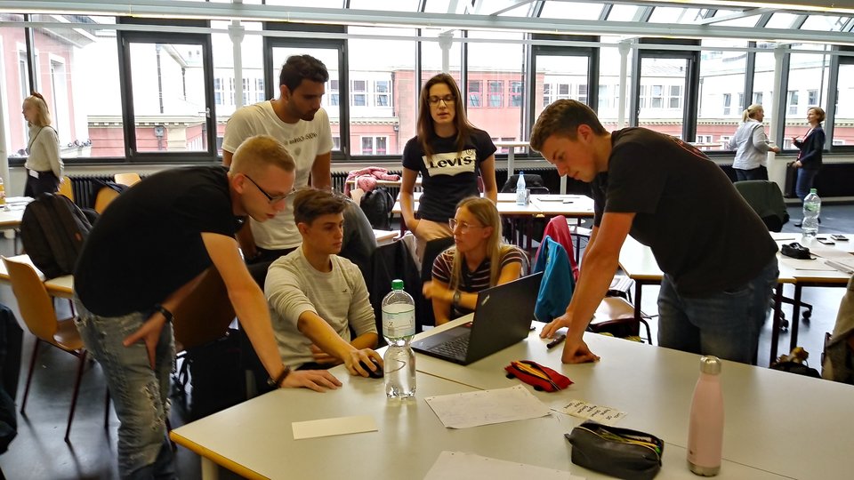 Sechs Studierende diskutieren vor einem Laptop