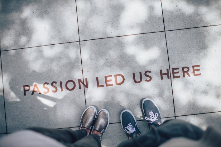 Zwei Menschen stehen auf dem Gehsteig vor einem Schriftzug, der lautet "Passion led us here".