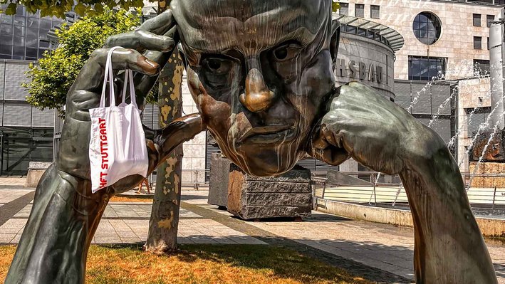Die Statue "Der Denker" in Stuttgart mit einem HFT Stuttgart Jute-Beutel an der Hand