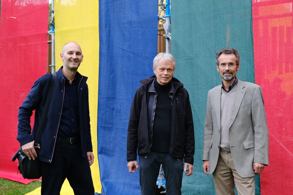 Porträt dreier Männer vor einem bunten Pavillon