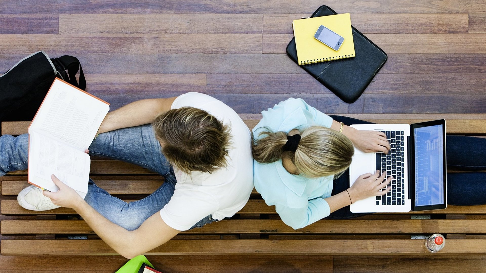 Zwei Studierende sitzen Rücken an Rücken und lernen