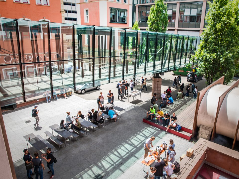 Studierende sitzen im Innenhof bei Sonnenschein zusammen