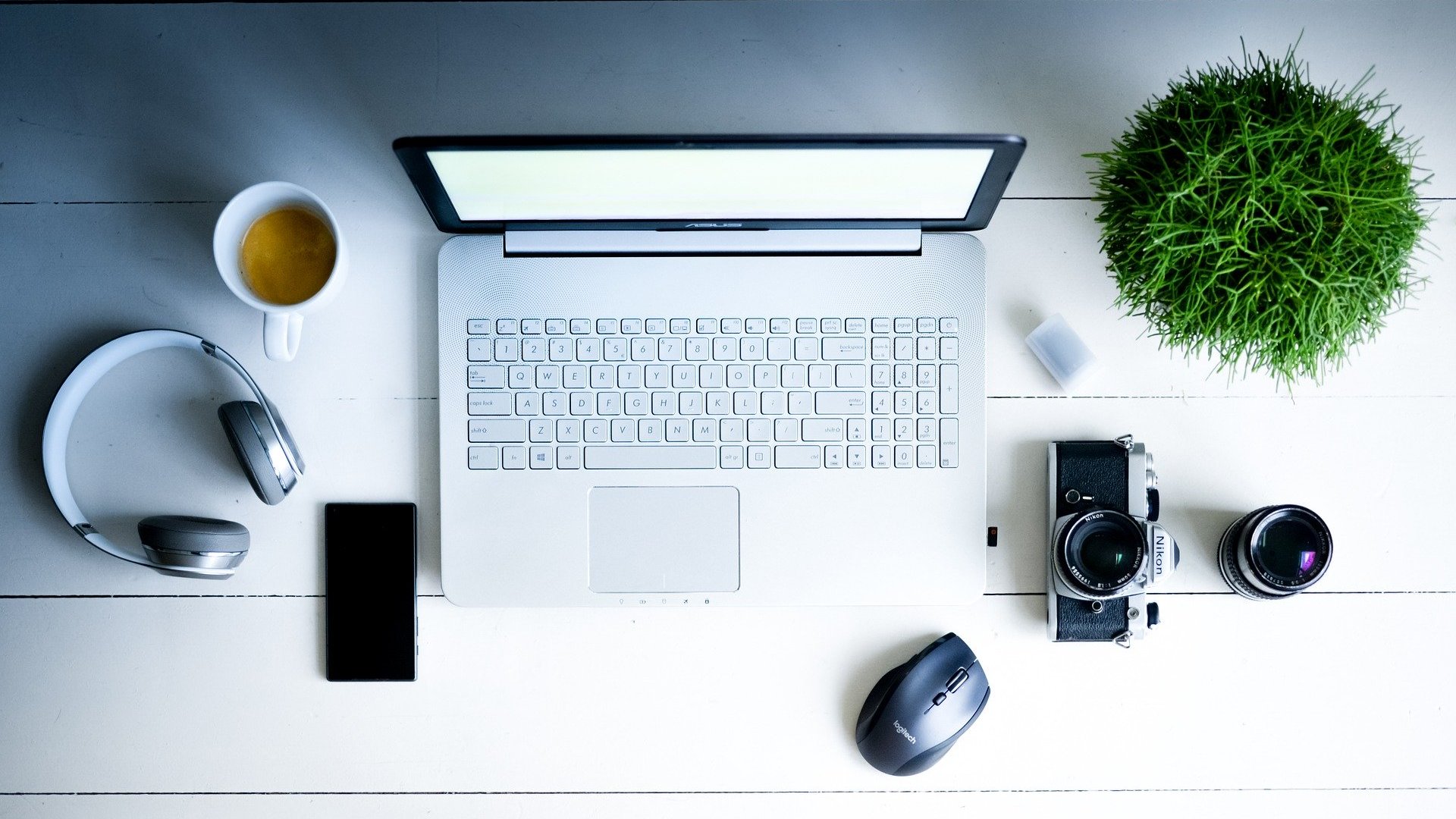 Arbeitsplatz mit Laptop, Handy, Kopfhörer, Fotoapparat, Kaffeetasse