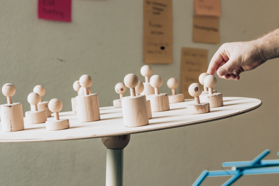 Auf dem Bild ist eine Platte zu sehen, die schief steht und auf der eine Hand eine Holz-Figur wegnimmt.